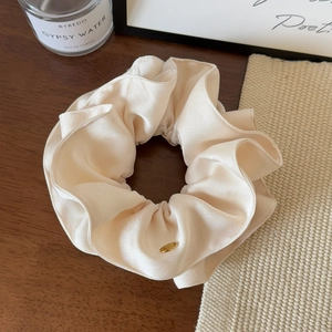Detailed close-up of cream satin scrunchie featuring elegant gold brand logo tag