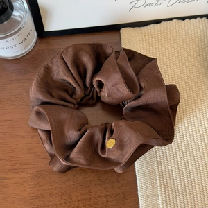 Macro shot of brown satin scrunchie with double-layered edges and gold logo detail