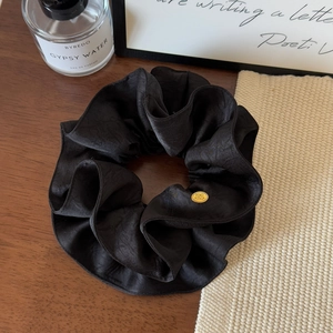 Detail shot of black satin scrunchie with elegant golden oval logo on wooden surface
