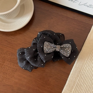 Detail of a large black mesh bow hair claw clip with sparkling rhinestones on wood