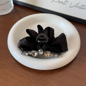 Détail de la grande pince à cheveux nœud en satin noir avec strass dans un plat céramique