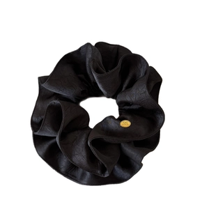 Elegant black double-layered fabric hair scrunchie with a gold logo plate on white background