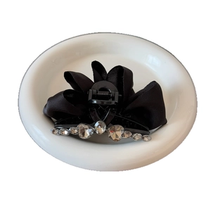 Pince à cheveux élégante en satin noir plissé avec strass sur une assiette blanche