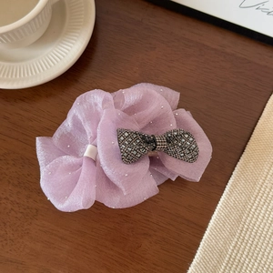 Macro shot of purple mesh ribbon hair claw with sparkling crystal bow on wooden table