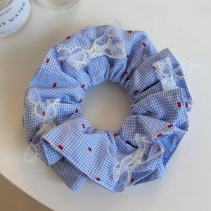 Détail d'un chouchou à carreaux bleus avec motifs cerises et bordure en dentelle blanche