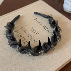 Detail of grey mesh headband with black spikes and crystals on a book surface