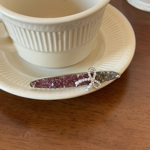 Detail view of purple crystal hair clip with white pearls and a rhinestone bow on ceramic saucer