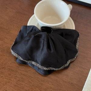Elegant black satin hair claw with sparkling rhinestone wavy edge on a wooden desk
