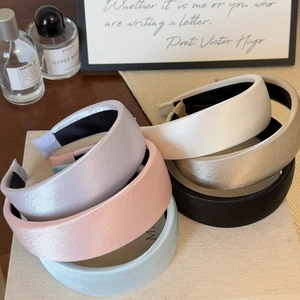 Detail of six pastel satin sponge headbands stacked on a beige textured display stand