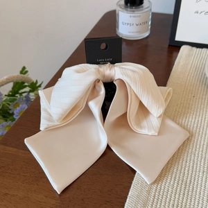 Détail d'une pince à cheveux chic avec nœud plissé crème sur un bureau en bois sombre