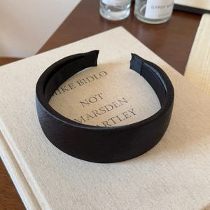 Detail of a black satin wide headband placed on an art book in a minimalist setting