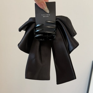 Détail d'une pince à cheveux à nœud en satin noir avec rubans et texture élégante