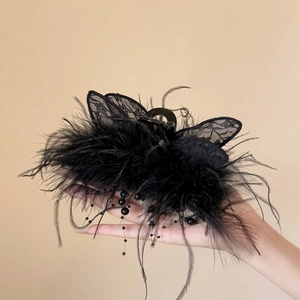 Détail d'une grande pince à cheveux noire avec plumes, ailes en dentelle et glands