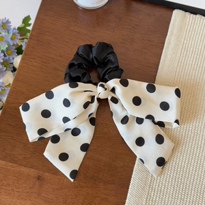 Close-up of black and white polka dot satin bow hair scrunchie on a rustic wooden desk