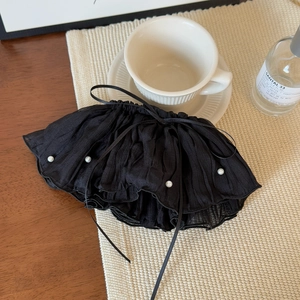 Close-up of elegant black pleated hair clip with pearls on a wooden desk with a coffee cup
