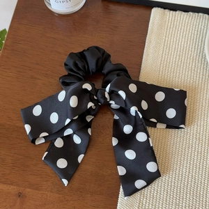Detailed macro view of black and white polka dot satin bow scrunchie on wooden background