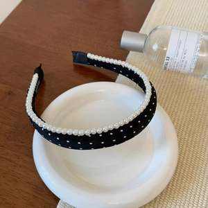 Close-up of black polka dot headband with pearls on a white plate with elegant props