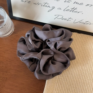 Detail of grey pleated satin oversized hair scrunchie on a decorative wooden table