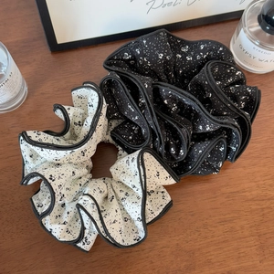 Close-up of black and white floral chiffon scrunchies on a wooden surface with decor