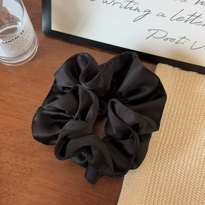 Macro shot of large black satin scrunchie on wooden desk with elegant props
