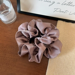 Close-up of a premium pleated satin scrunchie in coffee brown on a wooden desk