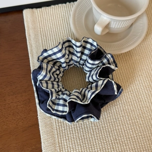Detailed shot of blue and white plaid fabric scrunchie on a woven mat with coffee cup