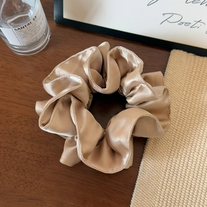 Close-up of champagne gold satin scrunchie with soft pleats on a dark wood background