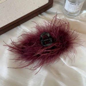 Detail showing fluffy burgundy ostrich feathers on a large claw clip with a sleek finish