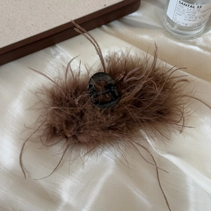 Detailed close-up of dark brown ostrich feather hair claw clip on soft white silk background