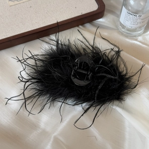 Detail of elegant black ostrich feather hair claw clip on white silk fabric background