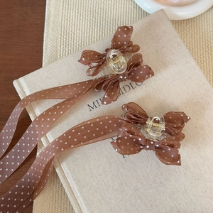 Détail de barrettes en mousseline à pois marron avec glands sur un livre en lin beige