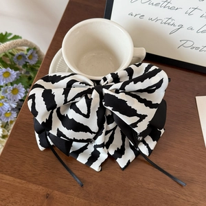 Elegant zebra stripe bow hair clip with black ribbons resting on a white coffee cup