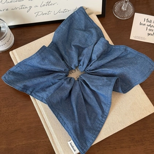 Detail view of deep blue denim scrunchie featuring a handmade woven label on wooden table