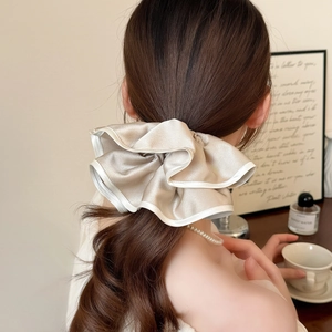 Détail d'un chouchou géant en satin champagne avec bordure blanche sur un modèle