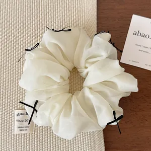 Close-up of white organza scrunchie with delicate black ribbon bows and pleated texture