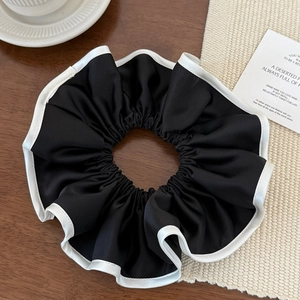 Gros plan sur chouchou en satin noir avec bordure blanche sur support tricoté
