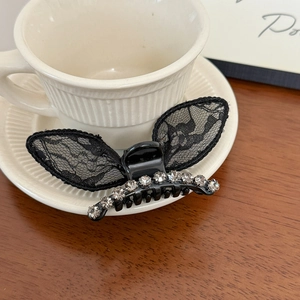 Detail of black lace bow hair claw clip with rhinestones on a coffee cup saucer