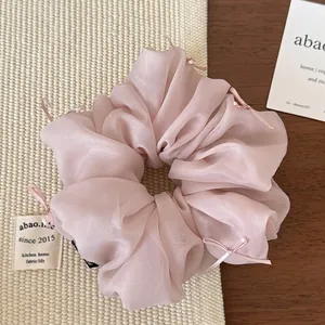 Detail view of light pink organza scrunchie with small ribbon bows on a textured background