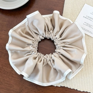 Détail du chouchou en satin champagne avec bordure blanche sur une table en bois