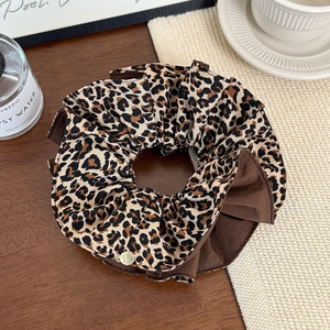 Détail du chouchou léopard avec tissu superposé et breloque dorée élégante