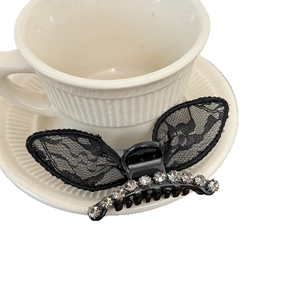 Elegant black lace hair claw clip with rhinestones shown on a ceramic tea saucer