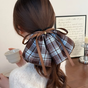 Plaid ribbon bow hair scrunchie with gold pendant shown on a ponytail in cozy indoor setting