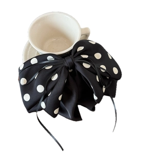 Elegant large black polka dot bow hair clip with ribbons on white ceramic cup