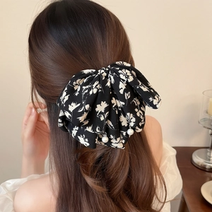 Floral print bow hair claw clip with pearl accents worn by a woman for an elegant hairstyle