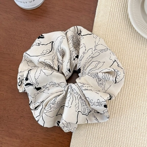 Detailed close-up of cream satin scrunchie with elegant black abstract line patterns