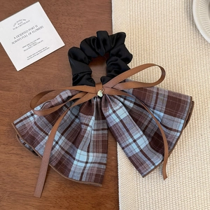 Detail of plaid bow hair scrunchie with a small metal heart pendant on wooden surface