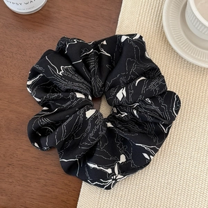 Detail of satin scrunchie with abstract white lines on black fabric on a wooden table