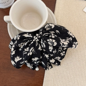 Floral print bow hair clip with pearl pendants on a rustic wooden tabletop