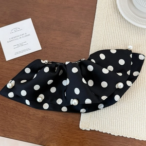 Detail of black polka dot satin hair clip with white faux pearls on wooden surface