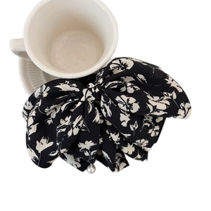 Floral bow hair clip with white pattern and pearl pendant on a ceramic background